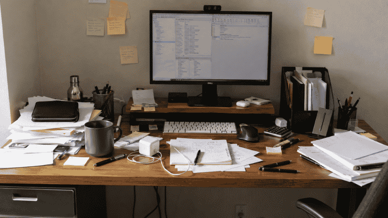 A messy office desk covered in papers, pens, cables, and random items before being organized