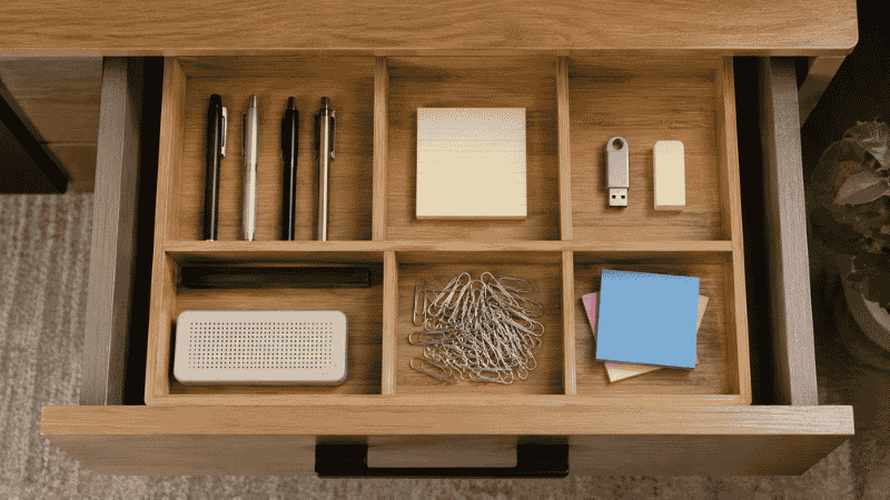 An open office desk drawer with a compartment organizer insert separating pens, paper clips, sticky notes, and small accessories into neat sections