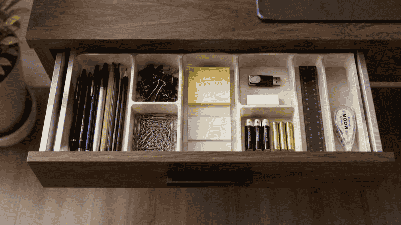An open desk drawer with a compartment organizer insert neatly separating pens, paper clips, sticky notes, and small accessories