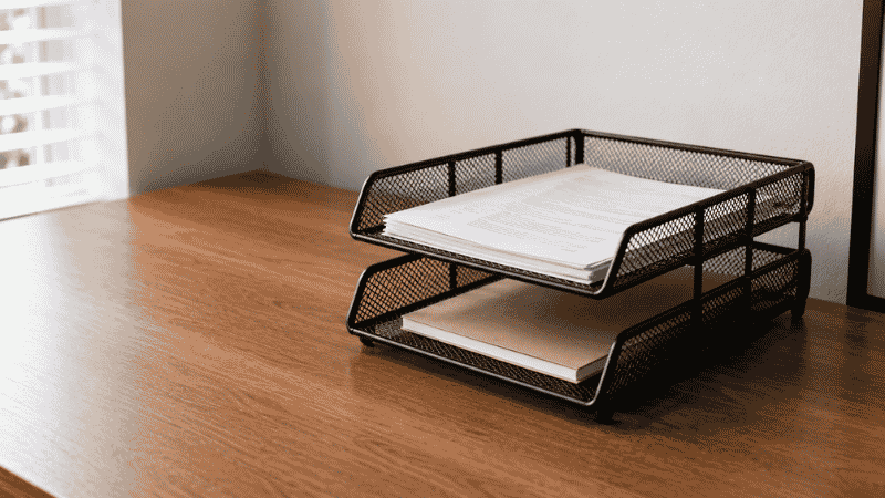 A two-tier metal letter tray on a desk neatly holding documents and papers in an organized incoming and outgoing system