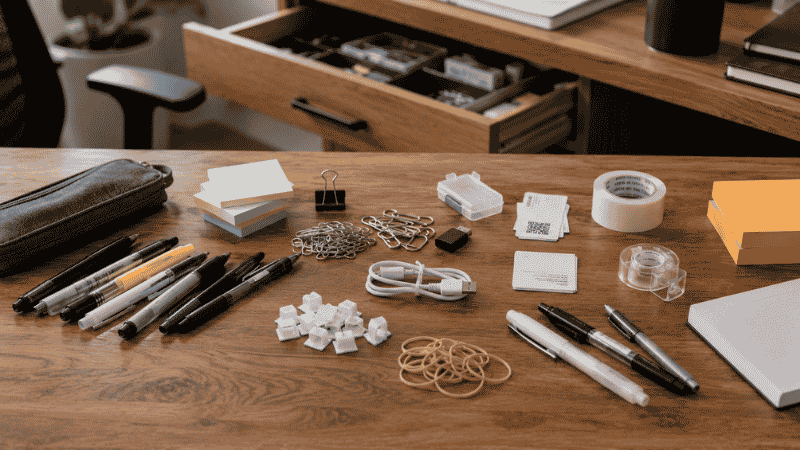 An open desk drawer with office supplies sorted into three piles on the desk surface during an audit — used, unused, and unknown items