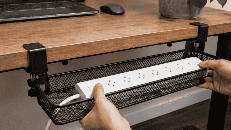 A cable tray being loaded with a power strip during installation under a desk showing the step of placing the power strip before routing cables