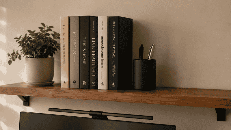 A desk shelf organized with books standing upright, a small plant, and a few office supplies with deliberate empty space showing proper organization