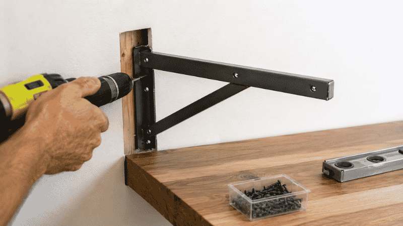 A wall-mounted desk bracket being installed into a wall stud during home office desk setup showing the mounting hardware and wall anchor