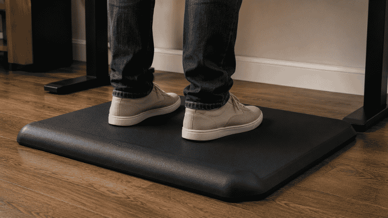 An anti-fatigue mat with raised ridge bar positioned in front of a standing desk showing the standing desk footrest solution