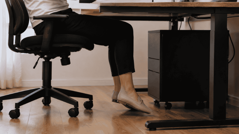 Feet slightly off the floor while seated at a desk showing the dangling feet problem that a footrest is designed to solve