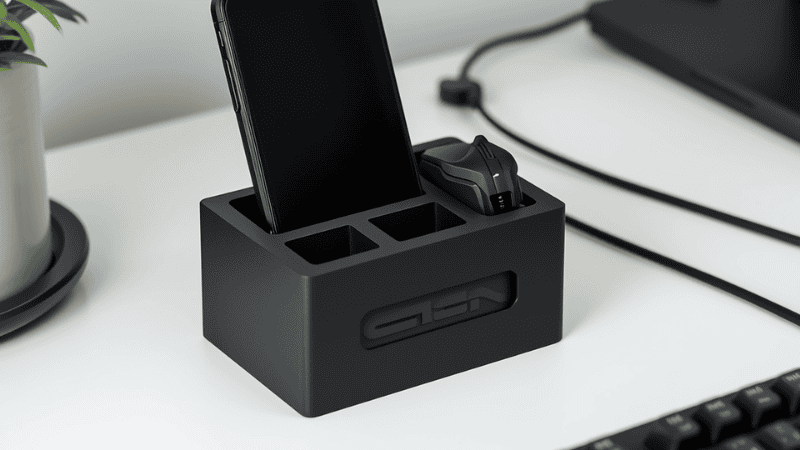 A high-angle shot of a minimalist workspace featuring a custom matte black 3D printed desk organizer holding an MX Master mouse, a mechanical keyboard cable, and a smartphone at a 15-degree ergonomic viewing angle