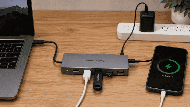 A powered USB hub with its own wall power adapter connected to a desk with multiple devices plugged in including a phone charging and external drive
