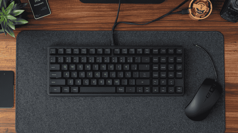 A professional workspace featuring a 75% mechanical keyboard on a walnut desk with a charcoal felt desk mat, illustrating an ergonomic and minimalist productivity setup.