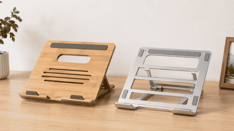 A side by side comparison of a wooden laptop stand on the left and an aluminum open-frame laptop stand on the right showing the material and design differences